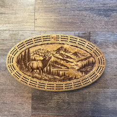 Handcrafted oval cribbage board featuring a bugling bull elk, a mountain landscape and a lake