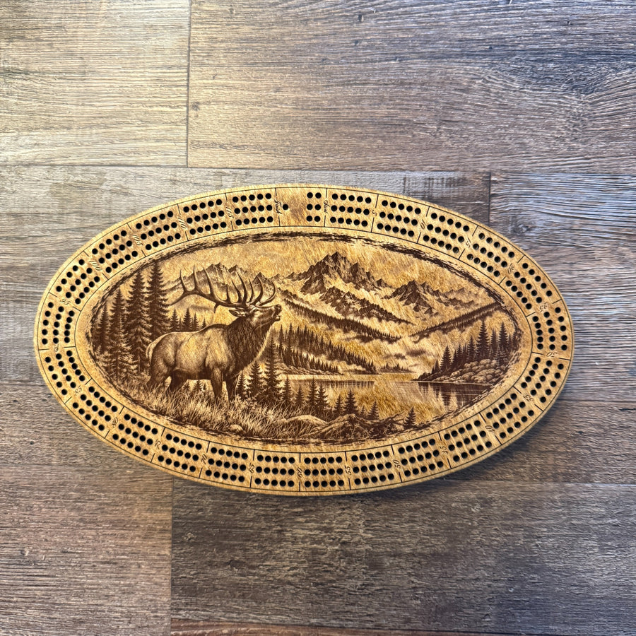 Handcrafted oval cribbage board featuring a bugling bull elk, a mountain landscape and a lake