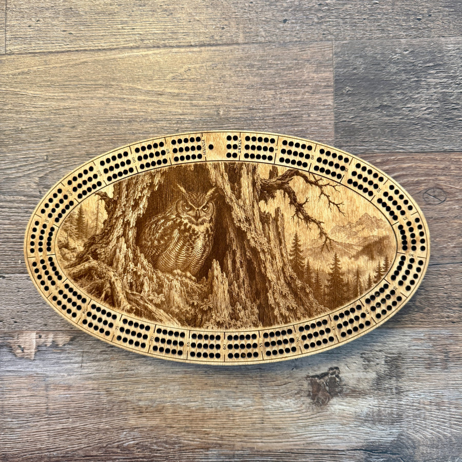 Oval wooden cribbage board featuring owl in hollow tree and mountain forest engraving